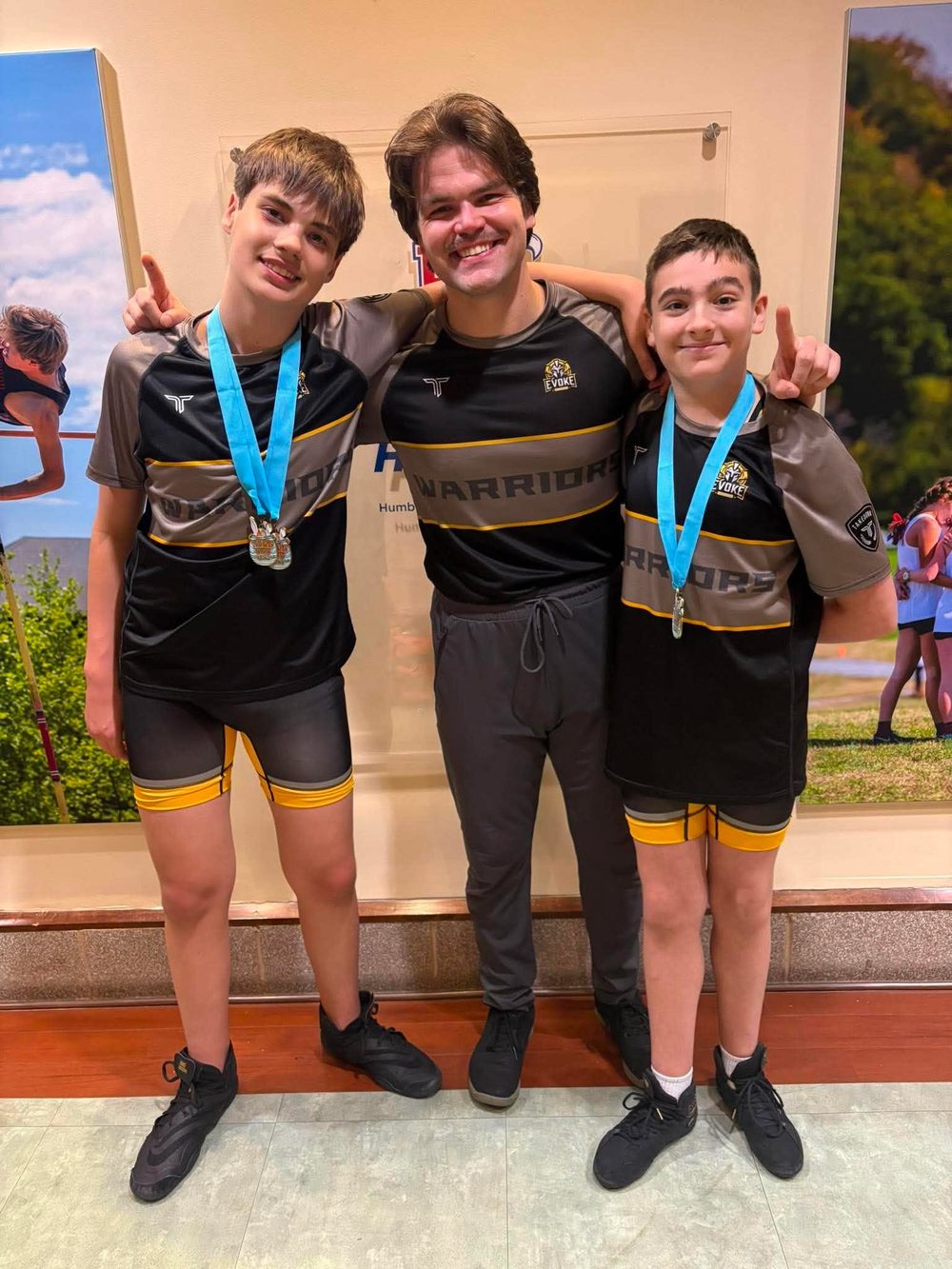 Coach Devan with two Warriors wrestlers wearing their tournament medals